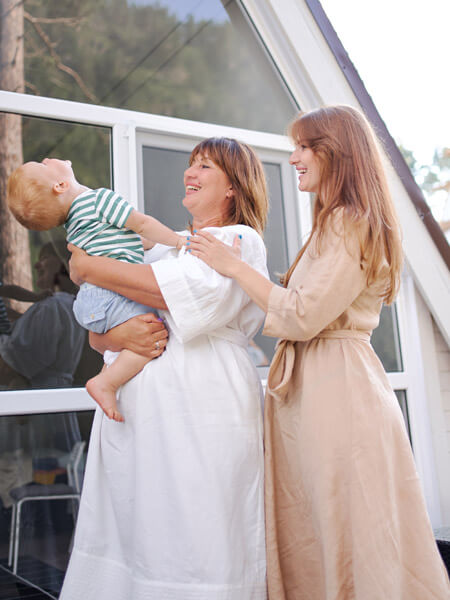 Image show a grandmother holding a baby while the mother stands by. Image is for CBG-Salbe CBG reduziert Muskelschmerzen